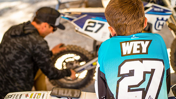 Vincent leaning on his motorcycle watching his dad work on his bike.